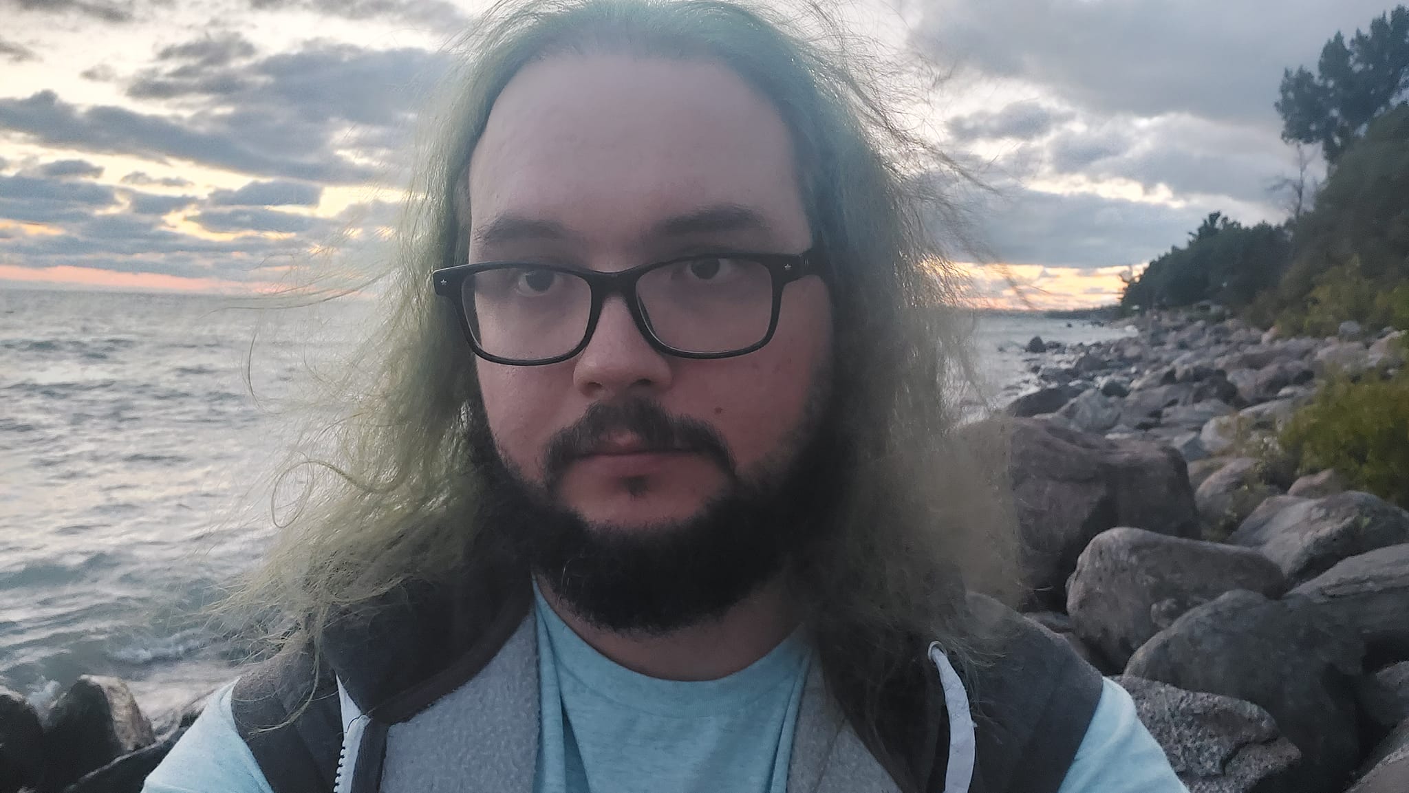 A man with green hair and a beard is outside after dark at the breakwater